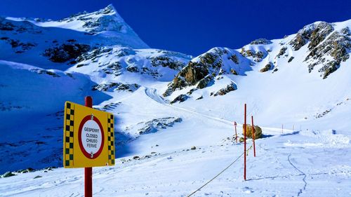 Information sign on snowcapped mountains against clear blue sky