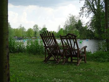 Chairs on tree by water against sky