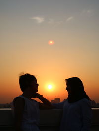 Silhouette people standing against orange sky during sunset