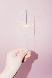 Cropped hand of woman holding sparkler against wall