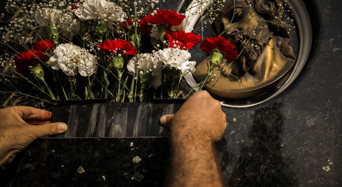 Close-up of hands offering bouquet of red and white flowers in cemetery