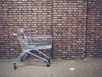 Shopping cart on sidewalk against brick wall