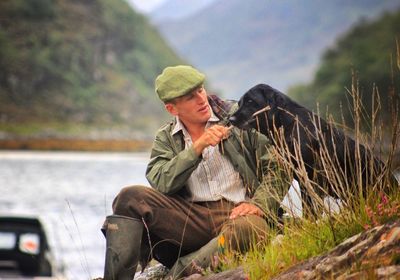 Young man sitting with dog at lakeshore