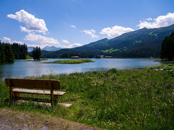 Bench by lake against sky