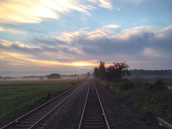 Railroad track on field against cloudy sky