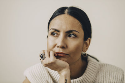 Woman wearing sweater with hand on chin against beige background