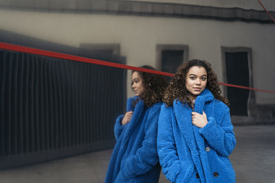 Portrait of young woman against blue wall during winter