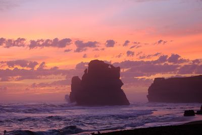 Silhouette rocks on shore against sky during sunset