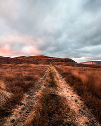 Dirt road amidst field against sky