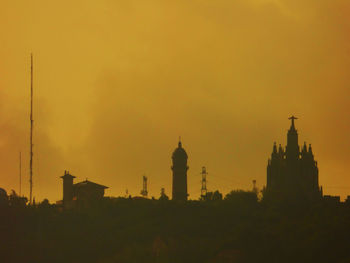 Distant view of silhouette temple expiatori del sagrat cor against orange sky