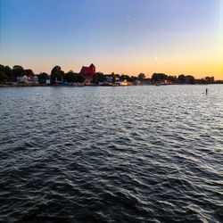 Sea by buildings against clear sky during sunset