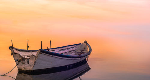 Boat moored at sea against sky during sunset
