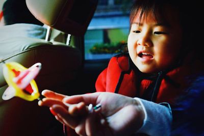 Cropped hand of woman holding toy by daughter traveling in car