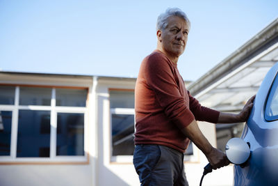 Senior man charging electric car on sunny day