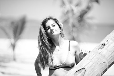 Portrait of smiling young woman wearing bikini top while standing at beach during sunny day