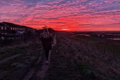 Rear view of girl walking on field against sky during sunset