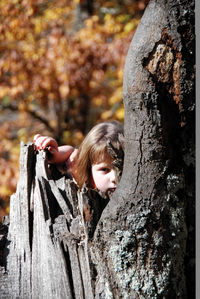 Portrait of girl looking through tree trunk