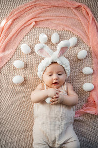 Newborn baby lies on a bed in pastel colors like an easter bunny on the grass with eggs