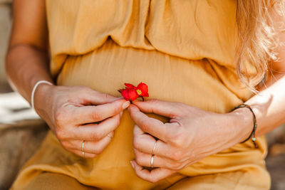 Midsection of pregnant woman holding flower while sitting outdoors