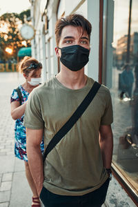 Young man walking along a store front in the city center in the evening wearing the face mask