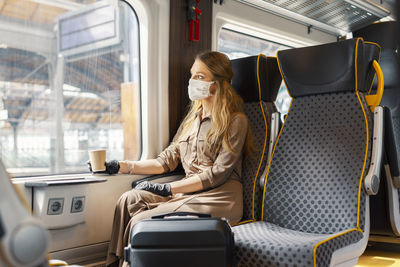 Woman wearing mask sitting on seat in train