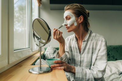 Beauty home facial skin care, a woman applies a clay cleansing mask on her face.