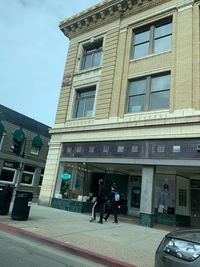 People walking by building in city against sky