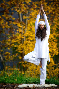 Full length of woman meditating against autumn tree
