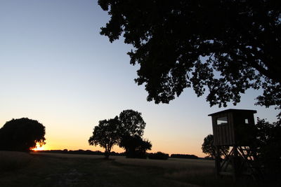 Silhouette trees on field against clear sky during sunset