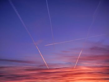 Low angle view of vapor trails in romantic sky during sunset