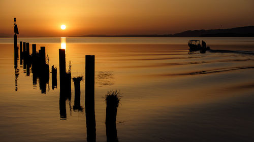 Silhouette wooden posts on beach against sky during sunset