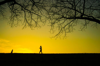 Silhouette man walking on field against sky during sunset