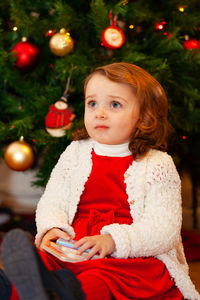 Cute girl sitting by christmas tree at home
