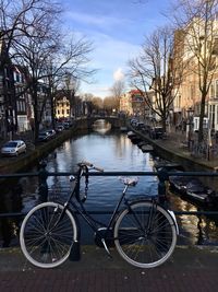 Bicycle parked by canal in city against sky