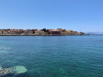 Sea by buildings against clear blue sky