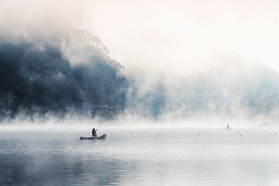 Silhouette fisherman fishing on boat in lake during foggy weather