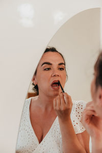 Mirror photo of beautiful young woman putting on makeup