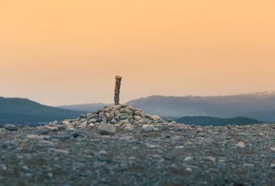 Cross on rock against sky during sunset