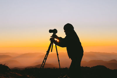 Silhouette man photographing at camera against sky during sunset