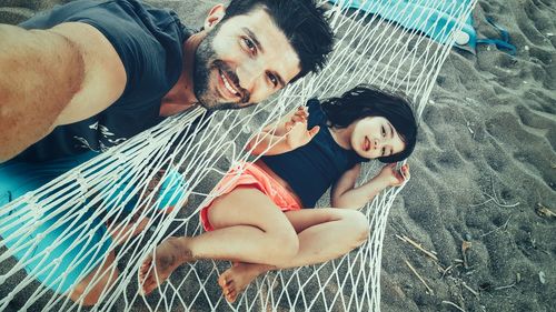 High angle portrait of man standing while daughter lying at hammock