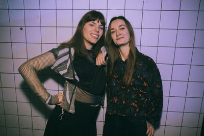 Portrait of smiling transgender woman with female friend standing against white wall at nightclub