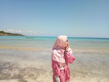 Smiling young woman standing at beach against sky