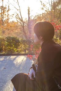 Woman carrying dog while sitting against plant