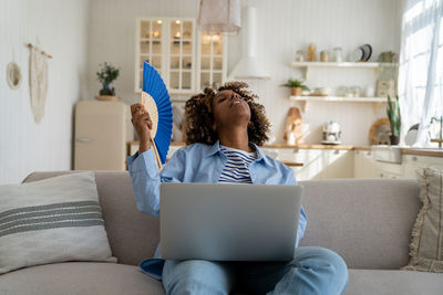 Young woman using laptop while sitting on sofa at home