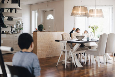 Father and daughter hiding behind chairs while gesturing to autistic son at home