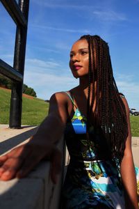 Young woman looking away while sitting against sky