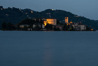 Illuminated buildings by sea against sky at dusk