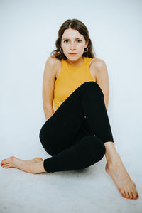 Full length portrait of young woman sitting on white background