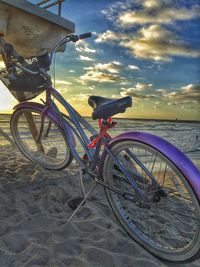 Bicycle parked on beach at sunset