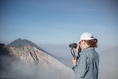 Woman photographing on mountain against sky